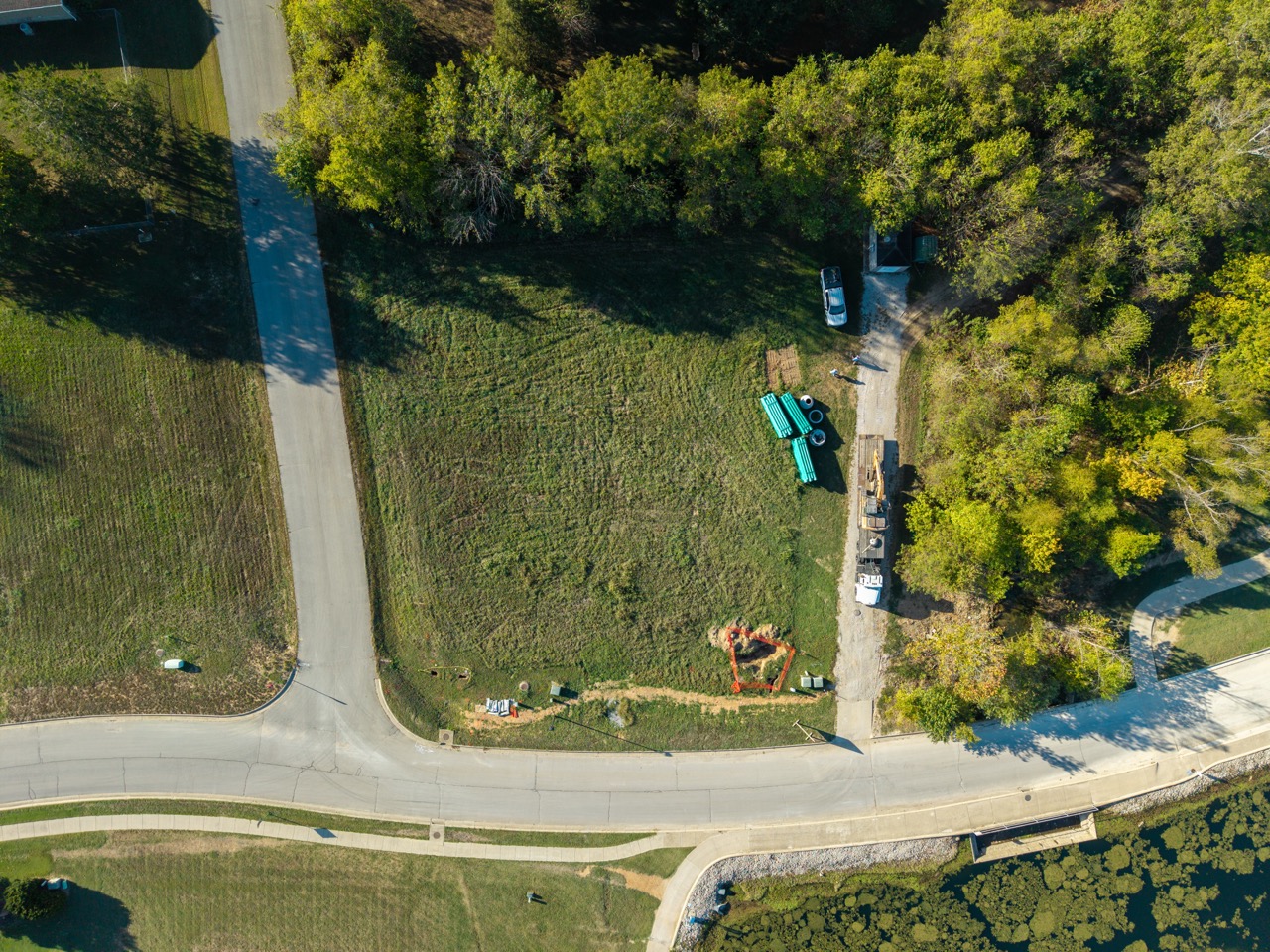 Green pipes stacked beside construction equipment along roadside.