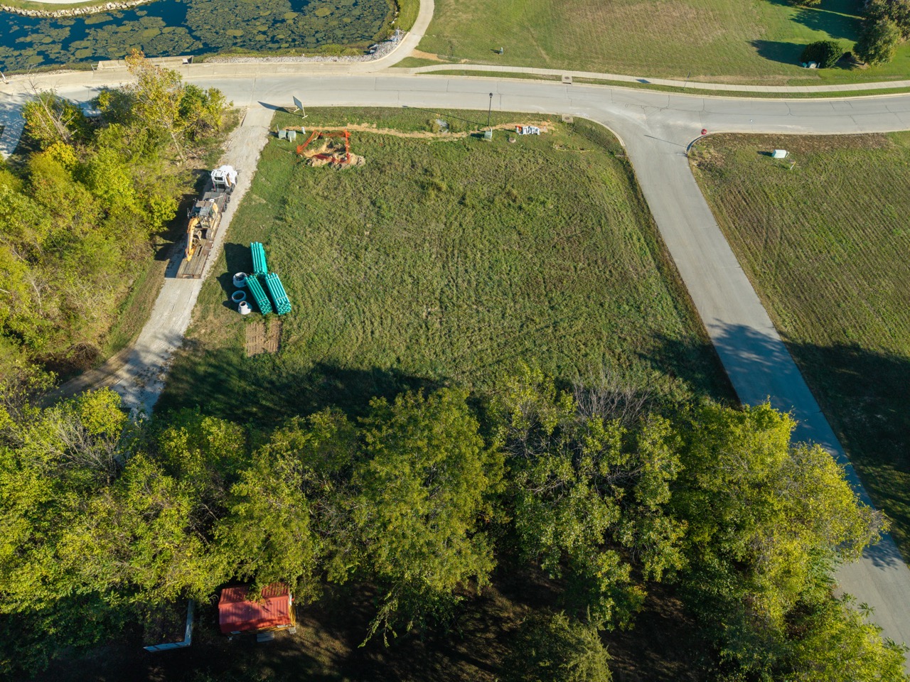 Construction equipment beside stacked teal pipes at construction site.