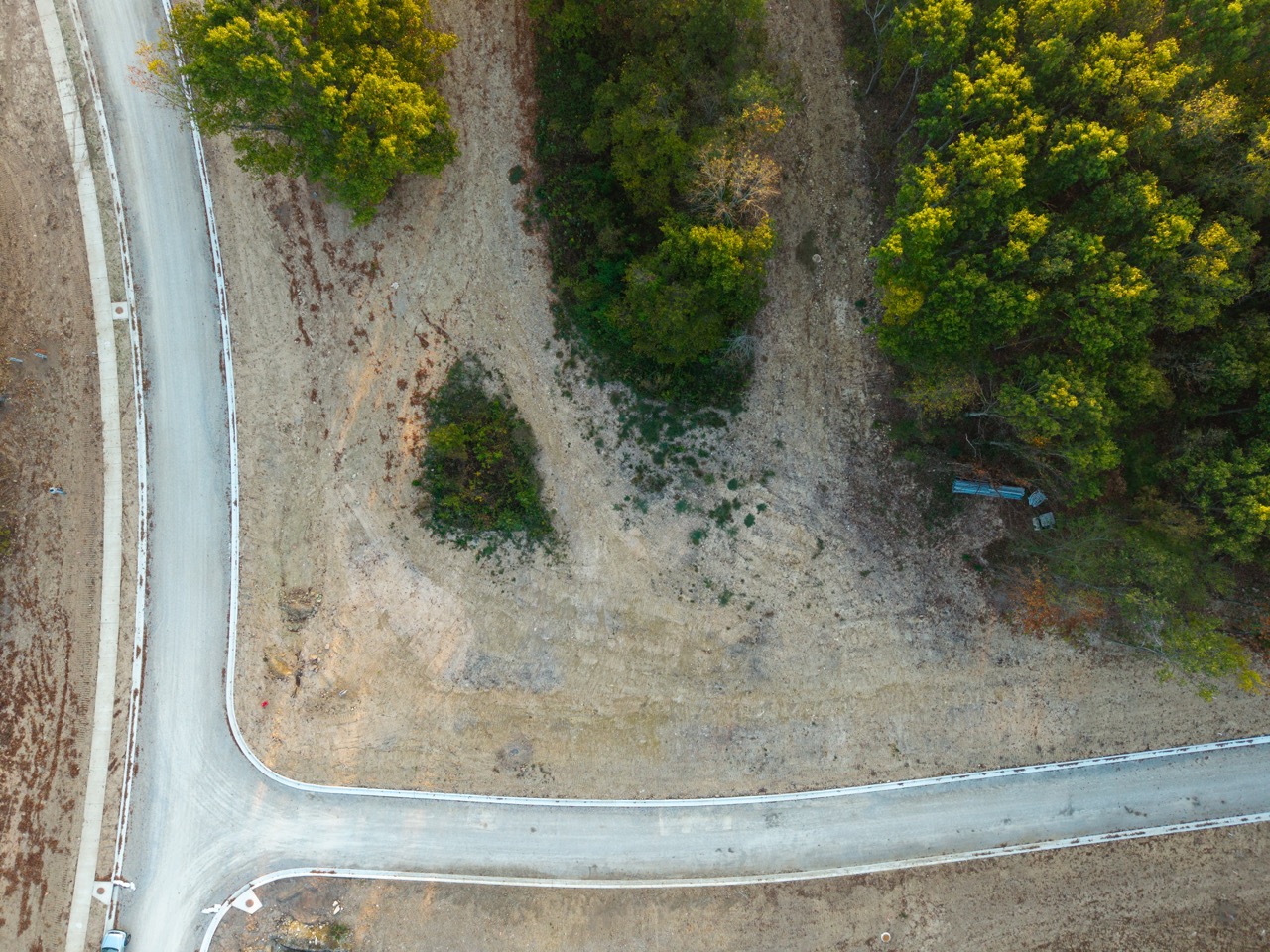 Aerial view of winding road beside dirt lot and trees