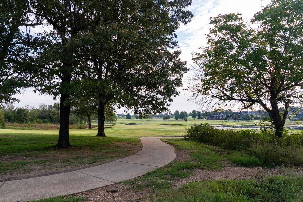 Curved paved path through trees toward golf course