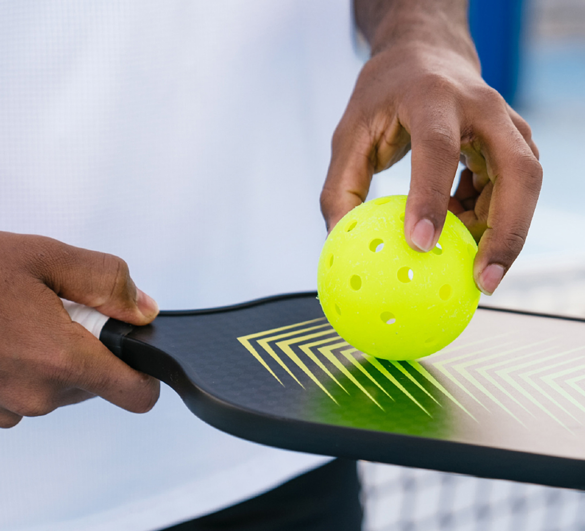 Neon yellow perforated ball held by fingers on paddle