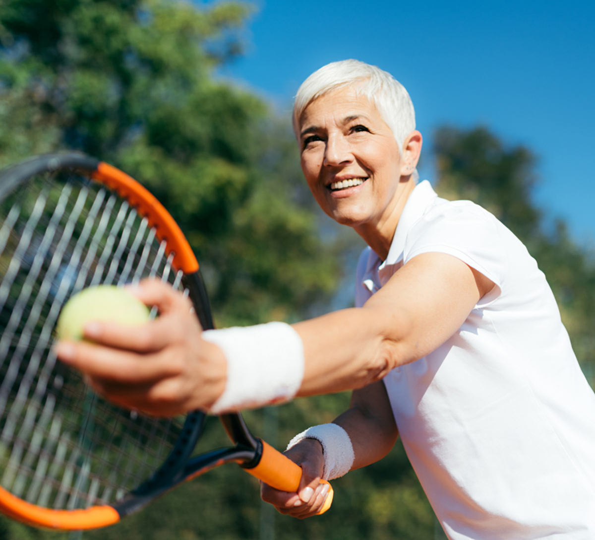 Older woman tennis player reaching for ball.