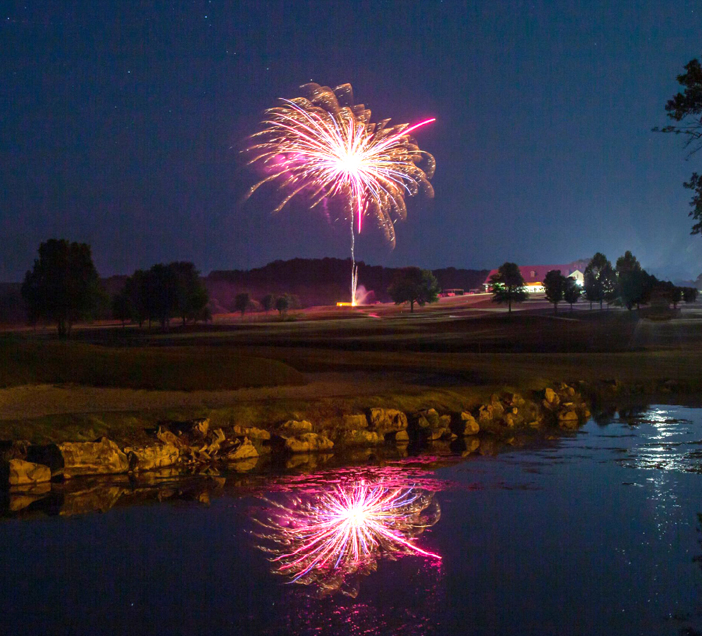 Fireworks bursting in night sky, reflected in water.